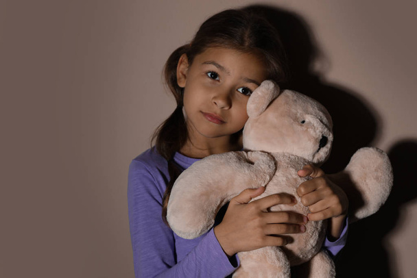 Sad little girl with teddy bear near beige wall. Domestic violen - Фото, зображення