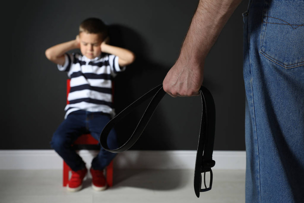Hombre amenazando a su hijo con cinturón en el interior, primer plano. Vía doméstica
 - Foto, imagen