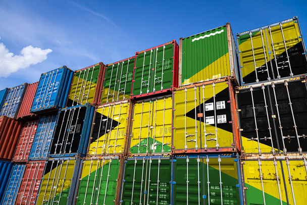 De nationale vlag van Jamaica op een groot aantal metalen containers voor de opslag van goederen gestapeld in rijen op elkaar. Begrip opslag van goederen door importeurs, exporteurs - Foto, afbeelding