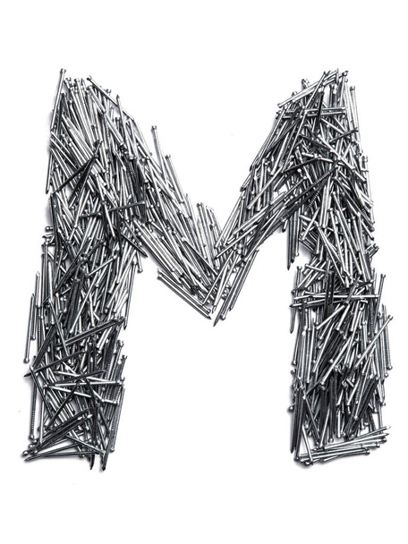 Letter M of the English alphabet from small iron nails  on a white isolated background. Industrial pattern of thin nails for fasteners. bright  numeral for design.  - Photo, Image