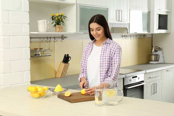 Beautiful young woman preparing lemon water in kitchen - Photo, image