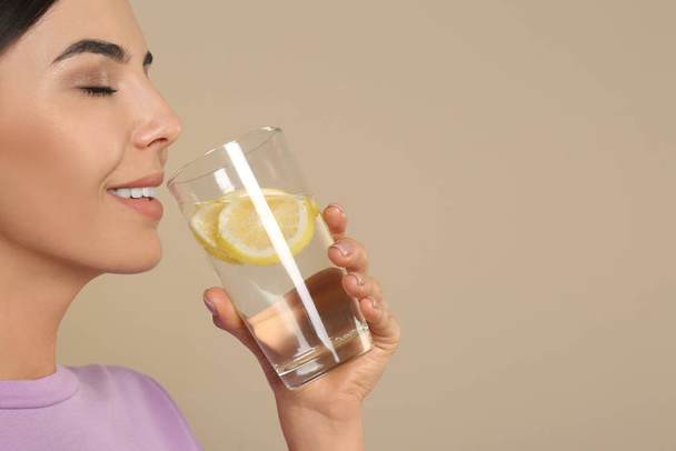 Beautiful young woman drinking tasty lemon water on beige backgr - Photo, image