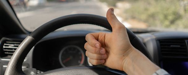 first person view of driver showing thumb up in front of steering wheel - Photo, Image