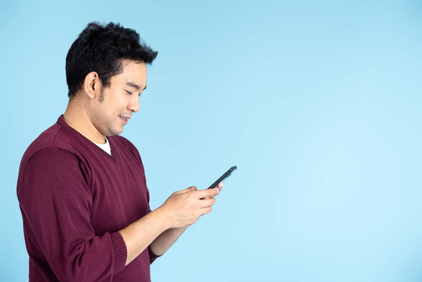 Happy Asian man wearing sweater using smartphone on blue backgro - Foto, Imagen