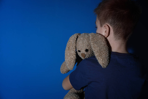 Sad little boy with toy near blue wall, space for text. Domestic violence concept - Photo, Image