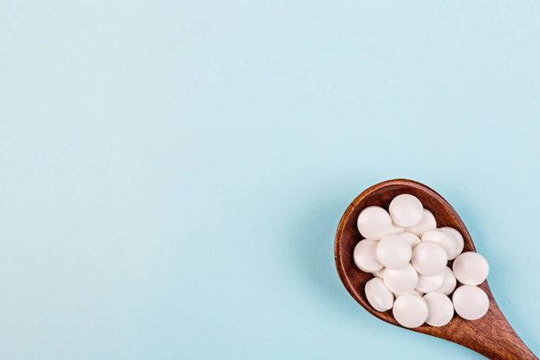 White pills in spoon on a pastel blue background. Flat lay, top view, overhead, mockup, template, copy space. Pharmacy and medical concept - 写真・画像
