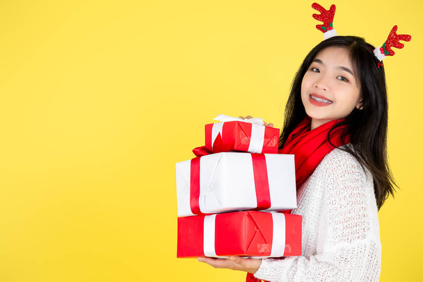 Happy Asian teenager girl holding gift boxes on yellow  backgrou - 写真・画像