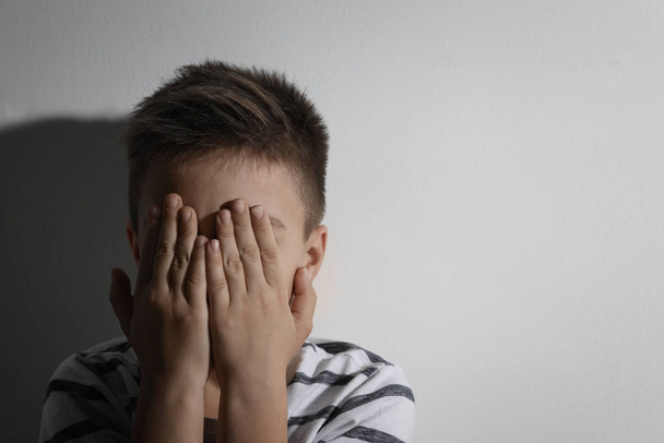 Scared little boy closing his eyes near white wall, space for text. Domestic violence concept - Foto, Imagen