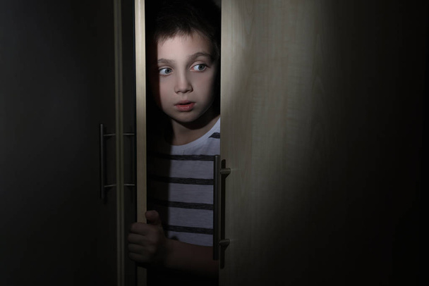 Scared little boy hiding in wardrobe. Domestic violence concept - Фото, изображение