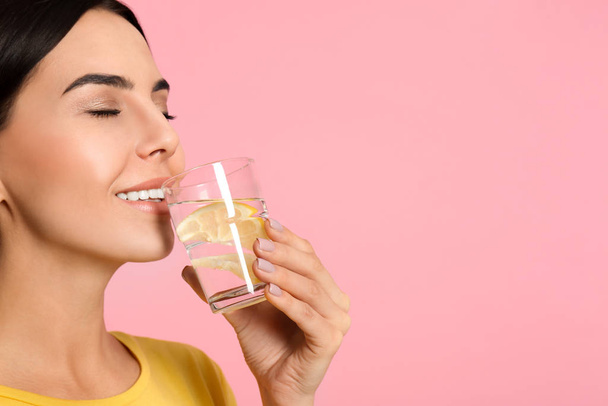 Beautiful young woman drinking tasty lemon water on pink backgro - Photo, Image