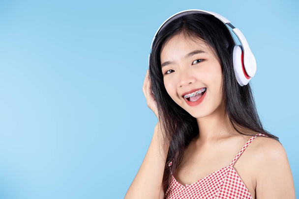 Happy Asian teenager girl using headphone on blue background. - Fotoğraf, Görsel