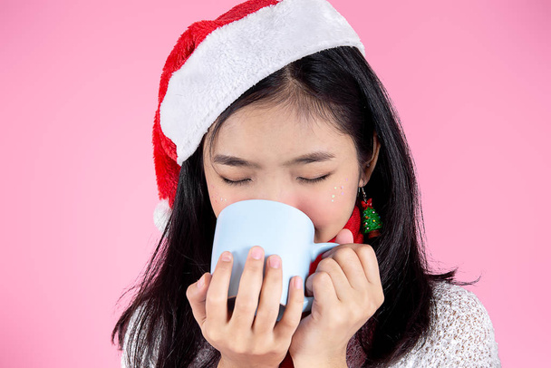 Asian teenager girl wearing Santa hat holding hot drink in her h - Фото, изображение