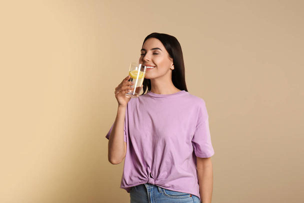 Beautiful young woman drinking tasty lemon water on beige backgr - Фото, изображение