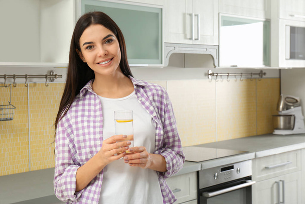 Beautiful young woman with lemon water in kitchen - Foto, afbeelding