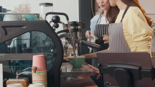 Beautiful young Asia lady barista working with coffee machine in coffee shop. Two small business owner Korean girl in apron making coffee by coffee machine with friend at counter in urban cafe. - Footage, Video