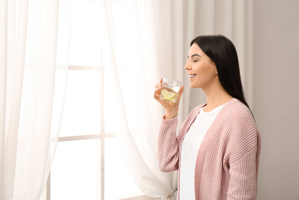 Beautiful young woman drinking fresh lemon water indoors - Foto, Imagen
