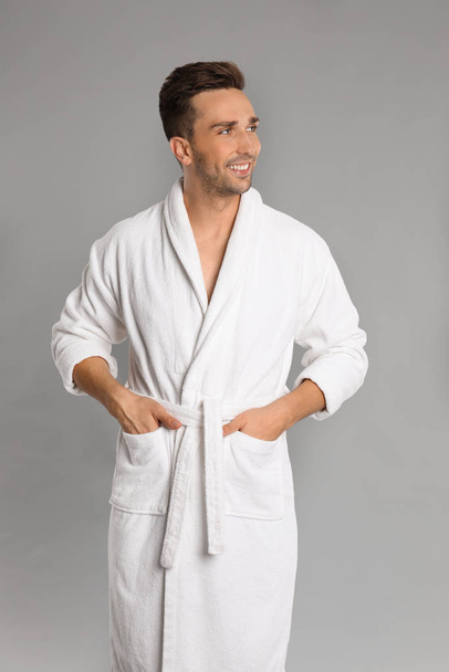 Happy young man in bathrobe on grey background - Foto, afbeelding