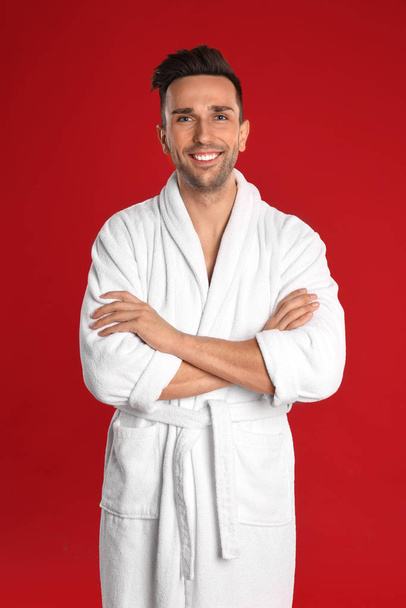 Happy young man in bathrobe on red background - Фото, зображення