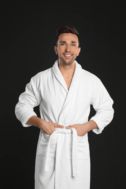 Happy young man in bathrobe on black background - Photo, image