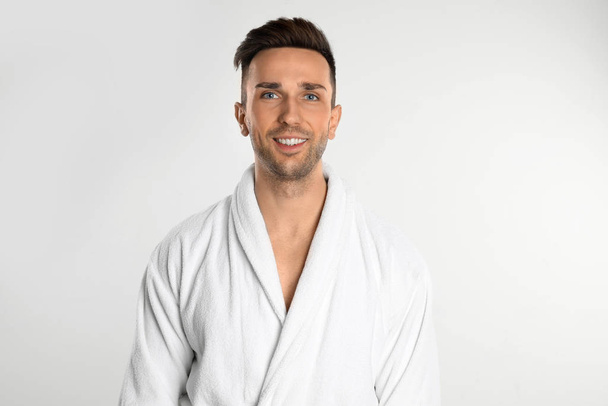 Happy young man in bathrobe on white background - Photo, image
