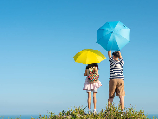 Back of boy and girl holding yellow and blue umbrella with top o - Photo, Image
