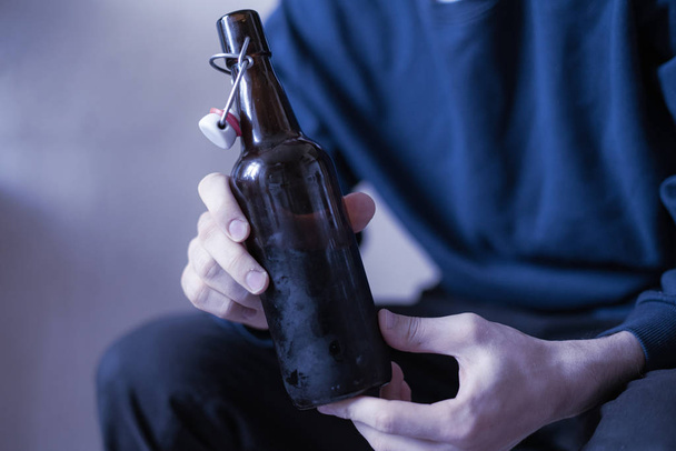 muž držící skleněnou láhev alkoholu sedící doma v depresi, problém se zlozvykem - Fotografie, Obrázek