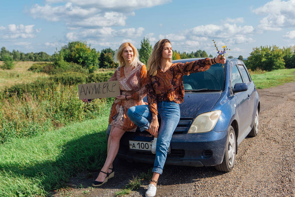 Two beautiful girls hitchhiking and vote with a sign ANYWHERE si - 写真・画像