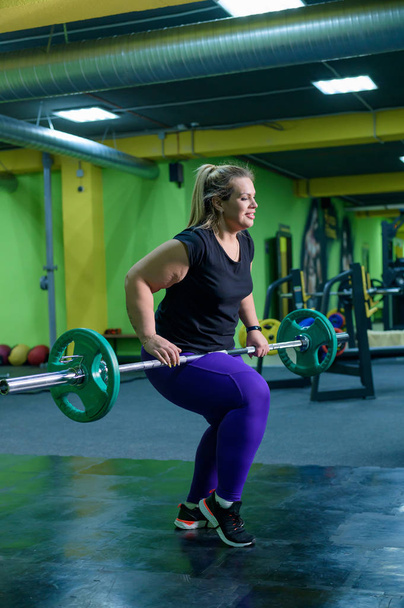 Fat European woman is engaged in fitness with a barbell in the gym. A fat girl does deadlift. - Fotografie, Obrázek