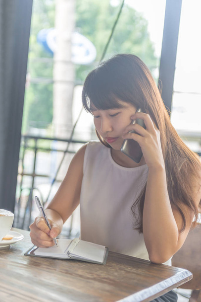 Asian girl talking on phone and writing notes - Φωτογραφία, εικόνα