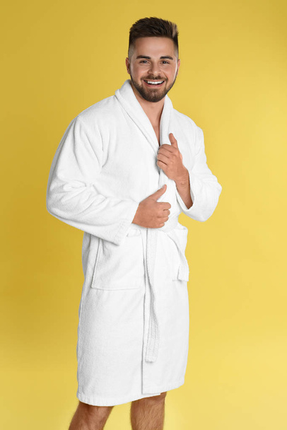 Happy young man in bathrobe on yellow background - Fotoğraf, Görsel