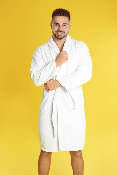 Happy young man in bathrobe on yellow background - 写真・画像