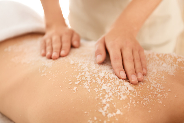 Young woman having body scrubbing procedure with sea salt in spa - Fotó, kép
