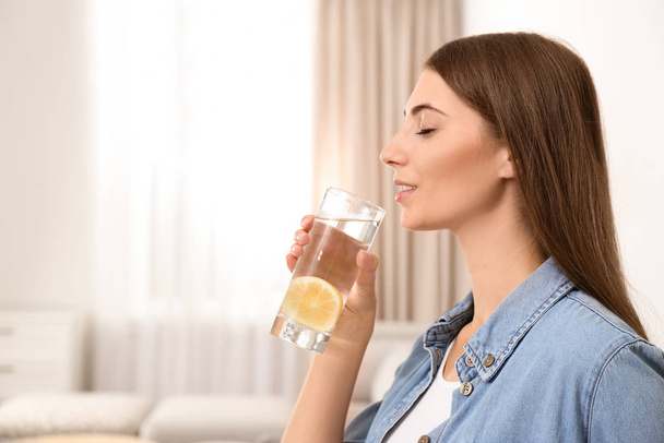 Young woman drinking lemon water at home. Space for text - Foto, Imagem