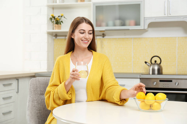 Young woman with glass of lemon water in kitchen - Valokuva, kuva