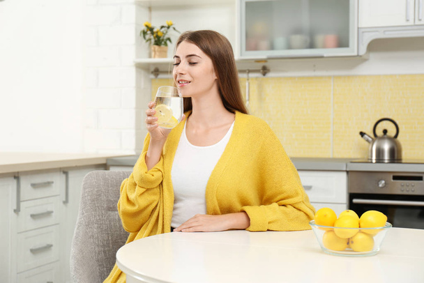 Young woman drinking lemon water in kitchen - Foto, Imagen