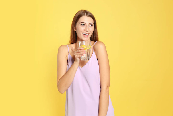 Young woman with glass of lemon water on yellow background - Foto, afbeelding
