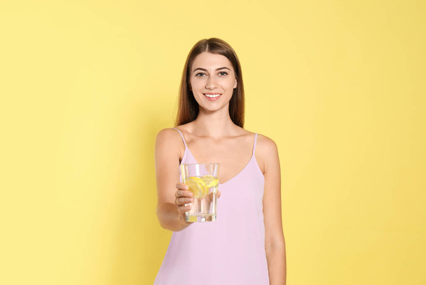 Young woman with glass of lemon water on yellow background - Фото, изображение