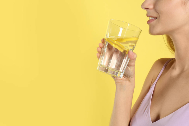 Young woman drinking lemon water on yellow background, closeup.  - Foto, afbeelding