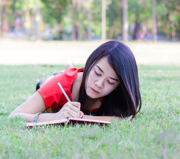 Beautiful young smiling woman lying on grass reading book - Фото, изображение