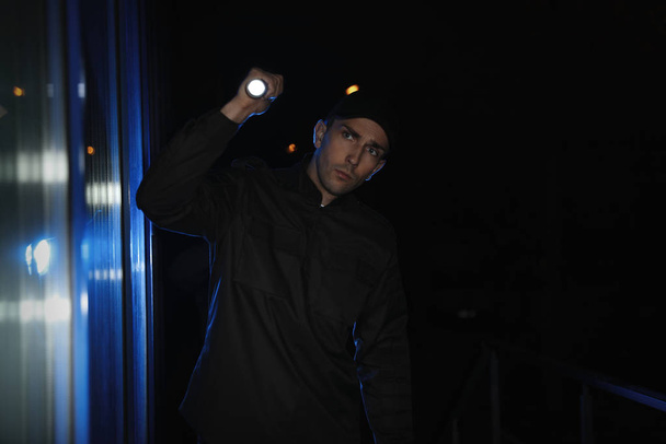 Male security guard with flashlight in dark corridor - 写真・画像