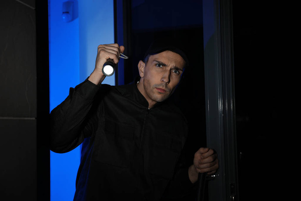 Male security guard with flashlight near entrance door at night - Фото, зображення
