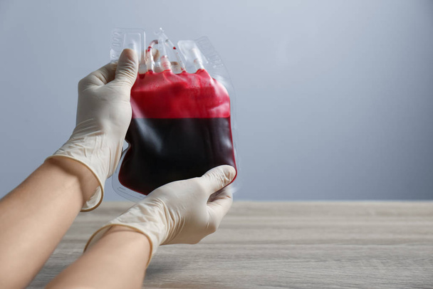 Woman holding blood for transfusion at wooden table, closeup with space for text. Donation concept - Fotografie, Obrázek
