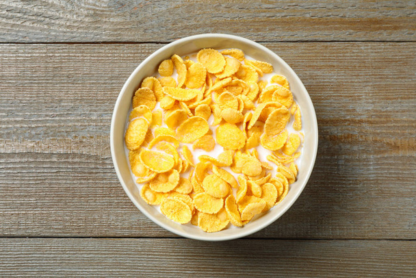 Tasty crispy corn flakes with milk on wooden  table, top view - Foto, afbeelding