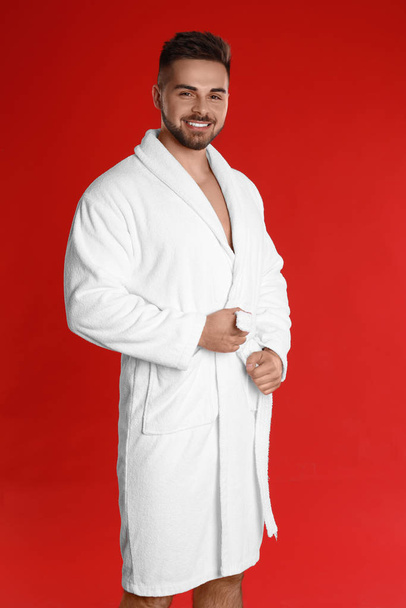 Happy young man in bathrobe on red background - Photo, image