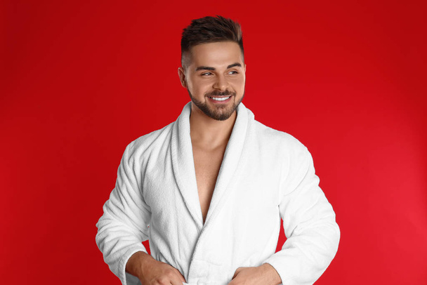Happy young man in bathrobe on red background - Foto, Imagen