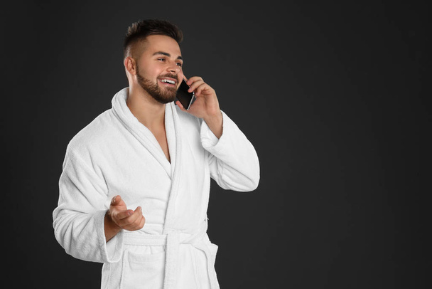 Hombre joven en albornoz hablando en el teléfono móvil contra la espalda negra
 - Foto, imagen