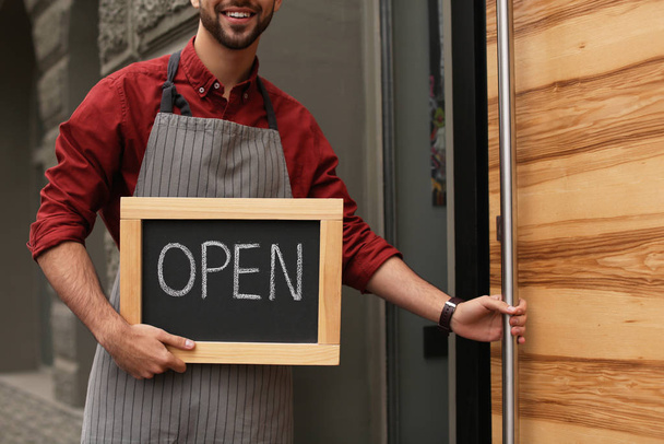 Young male business owner holding OPEN sign near his cafe, closeup - Foto, Bild