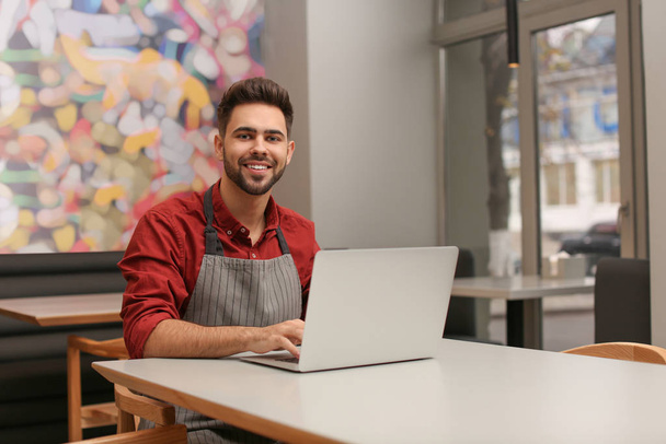 Young male business owner working with laptop in his cafe - Photo, Image