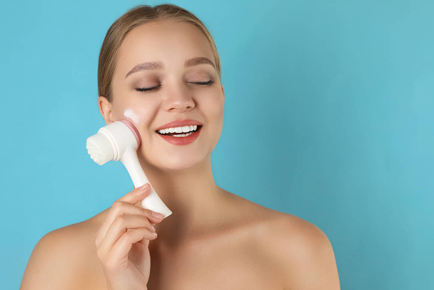 Young woman washing face with brush and cleansing foam on light  - Photo, Image