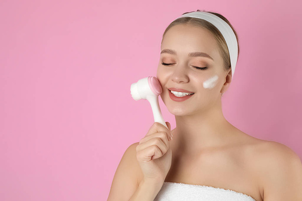 junge Frau wäscht Gesicht mit Pinsel und Reinigungsschaum auf rosa B - Foto, Bild